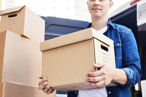 Mid-section portrait of young man holding cardboard box while unloading moving van outdoors