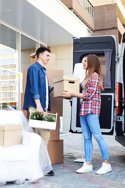 Side view portrait of young happy woman unloading boxes from moving van handing them to smiling husband
