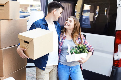 Portrait of happy young couple embracing  looking at each other tenderly while loading cardboard boxes to moving van outdoors