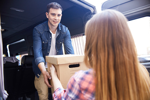 Portrait of happy young man taking cardboard boxes from his wife and loading them into moving van