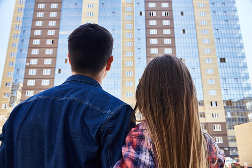 Back view portrait of young couple embracing looking at new apartment building, before moving in