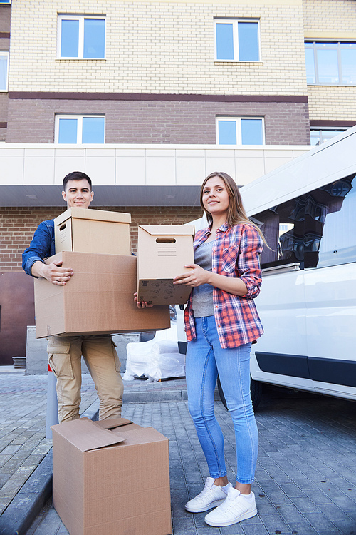 Portrait of happy young couple holding cardboard boxes posing outdoors  while moving into new apartment