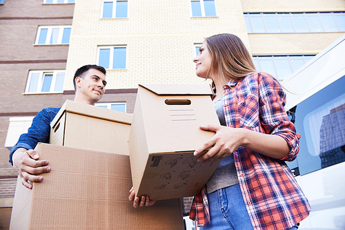 Low angle portrait of happy couple holding cardboard boxes while moving into new home, outdoors