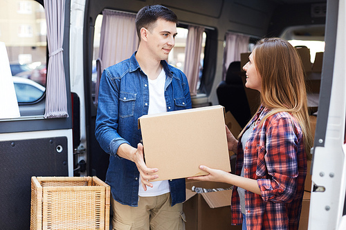 Portrait of smiling young man and woman unloading boxes from moving van outdoors