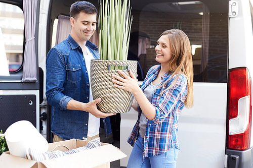 Portrait of happy young couple moving in new home, holding house plant and smiling outdoors
