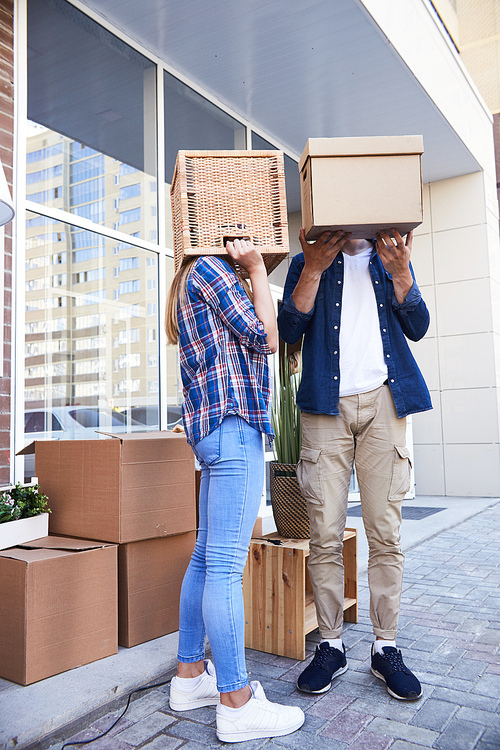 Portrait of unrecognizable young couple with boxes on heads having fun while unloading moving van outdoors