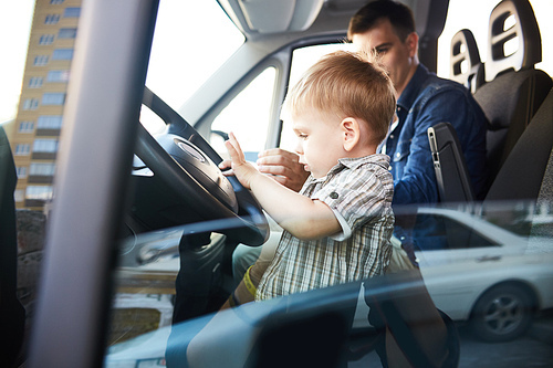 Portrait of cute little kid pressing the horn button on wheel sitting on front seat of car with dad