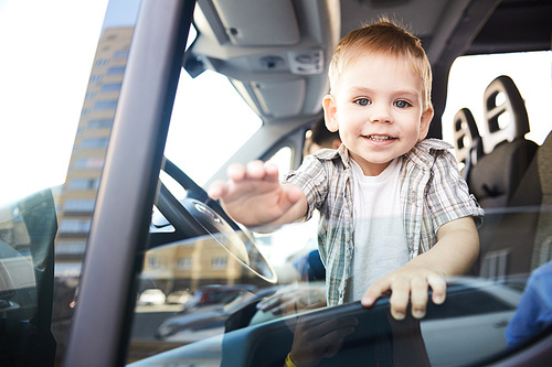 Portrait of cute little kid looking out of car window and smiling happily in sunlight