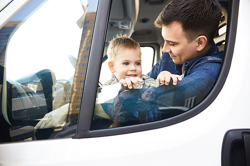 Portrait of cute little kid looking out of car window and smiling happily sitting on fathers lap