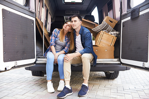 Portrait of pensive young couple sitting in the back of moving van resting after packing up