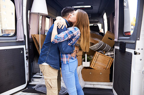 Portrait of loving young couple embracing happily standing by moving van with boxes  outdoors