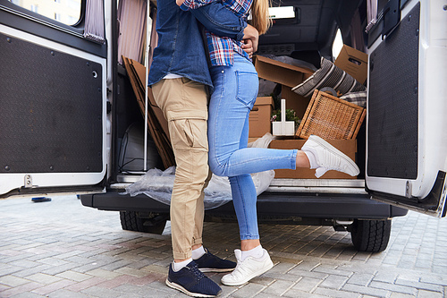 Legs of unrecognizable young couple embracing happily standing by moving van with boxes  outdoors
