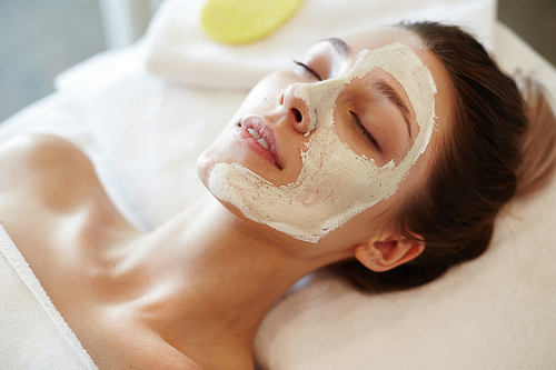 Closeup portrait of blissful young woman enjoying beauty treatments and face masks in SPA, lying on massage table with eyes closed