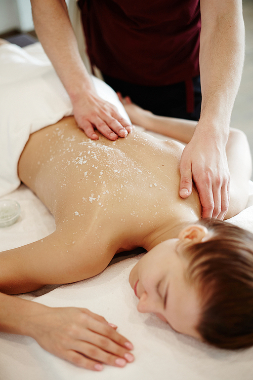 Closeup of unrecognizable male masseur rubbing back of young woman lying on massage table with eyes closed