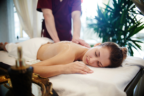 Portrait of relaxed young woman enjoying massage in SPA center, lying on massage table with eyes closed