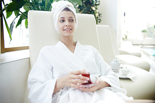 Portrait of beautiful young woman smiling  relaxing in lounge chair by swimming pool wearing bath robe and towel on head