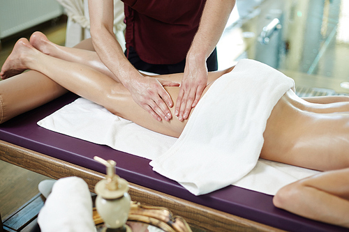 Unrecognizable man massaging legs of young woman lying on massage table in SPA center