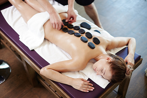 High angle portrait of young woman enjoying stone therapy lying on massage table in SPA center