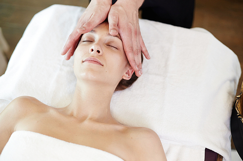 Above view portrait of young woman enjoying face lifting massage lying with eyes closed in SPA center and relaxing