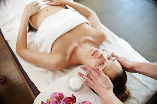 Portrait of beautiful young woman lying on massage table in SPA Center enjoying face massage and smiling blissfully