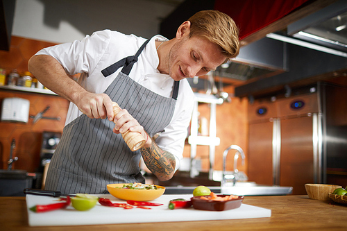 Portrait of handsome professional chef salting dish while cooking in restaurant kitchen, copy space