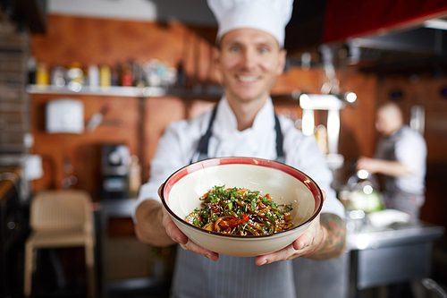 Portrait of proud professional chef presenting Asian food dish, focus on foreground