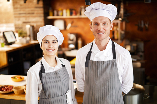 Waist up portrait of two professional cooks posing in restaurant kitchen smiling at camera, copy space