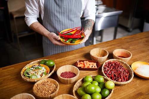 Mid section portrait of professional chef holding chili peppers and spices while cooking in restaurant kitchen, copy space