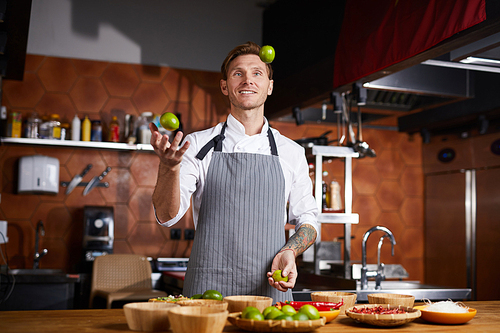 Portrit of handsome chef juggling limes standing at table with spices, copy space