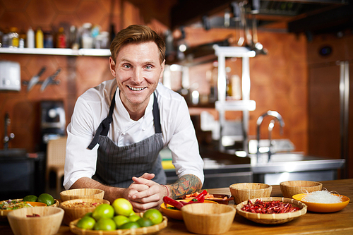 Waist up portrit of handsome chef posing in kitchen at table with spices, copy space
