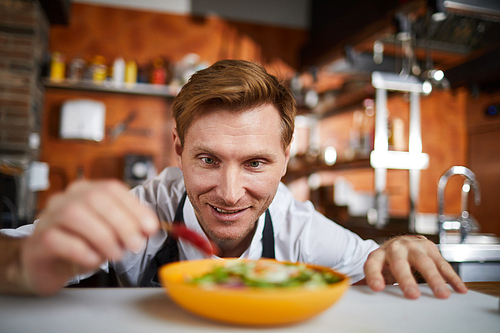 Portrait of excited chef putting hot chili pepper in salad, copy space
