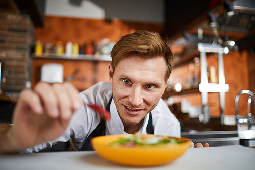 Portrait of excited male chef putting hot chili pepper in salad, copy space