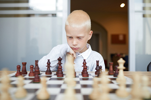 Thoughtful schoolboy playing chess, carefully thinking about his next move and analyzing strategy of opponent