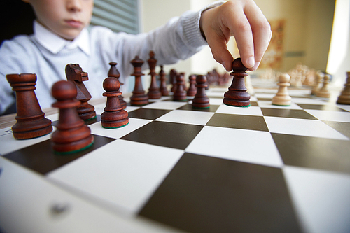 Hand of schoolboy in white shirt making indecisive chess move in response to move of opponent