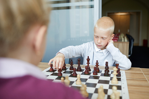 Blonde schoolboy in white shirt making chess move in response to chess move of girl in purple sweater