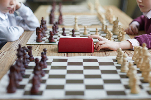 Schoolgirl in purple sweater playing chess with schoolboy and pressing chess clock after her move