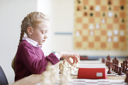 Girl with braided red hair in purple sweater playing chess alone and learning chess strategy