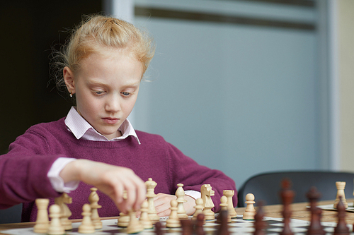 Girl with braided red hair in purple sweater playing with imaginary opponent and practicing chess strategy