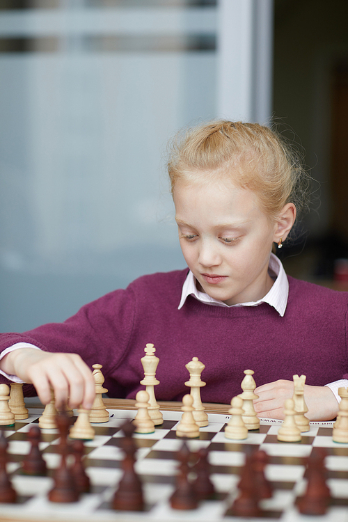 Girl with braided red hair in purple sweater studying chess figures and how they can move