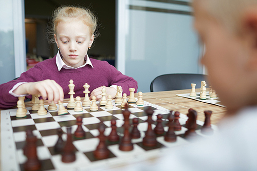 Schoolgirl with braided hair in purple sweater and white shirt carefully thinking about what chess move to make