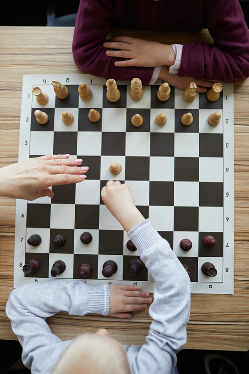 Hand of teacher above chess board preventing boy from making wrong, thoughtless chess move