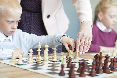 Boy in white shirt and girl in purple sweater learning to play chess in chess class at school