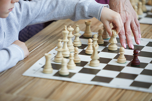 Hand of teacher showing boy in gray sweater chess move on chess board which can help to win