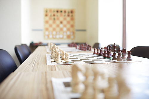 Long beige table covered with chess boards and surrounded by chairs in chess classroom at school