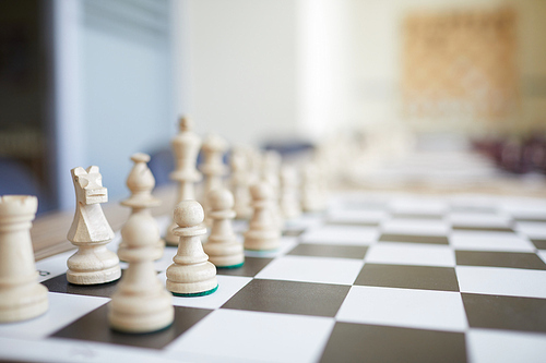 Black and white chess board with white wooden figures on table with blurred background