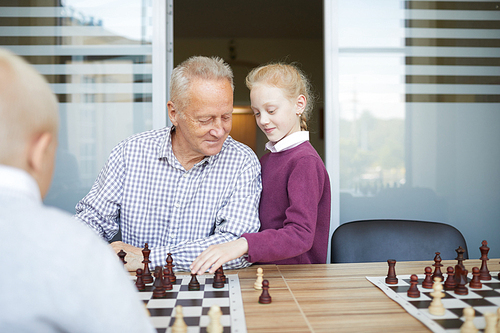 Small girl with red braided hair helping her grandfather to win chess game against her brother