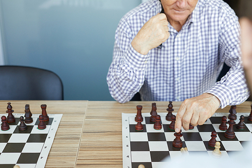 Concentrated old man in checked shirt making deliberate chess move in game during chess tournament