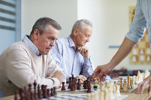 Two aged men with silver hair spending leisure time at chess club by playing chess with local grandmaster