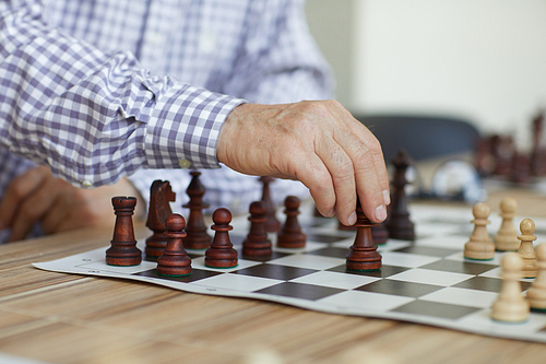 Tanned wrinkled hand of old professional grandmaster making decisive chess move during intense game