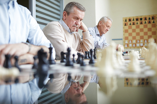 Long chess table in classroom at chess club with three chess players sitting in row next to different chess boards